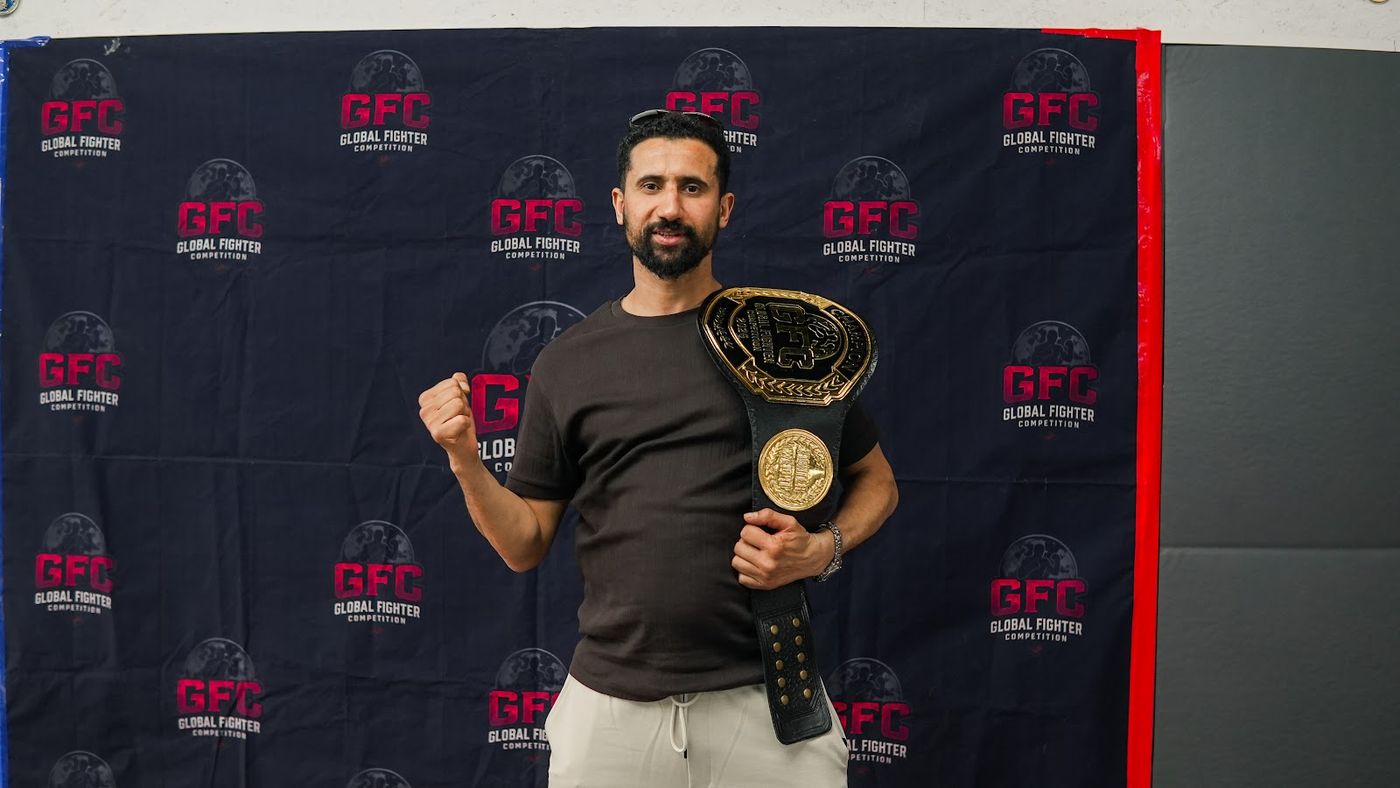 Trainer mit zwei Meisterschaftsgürteln vor dem Banner der Global Fighter Championship