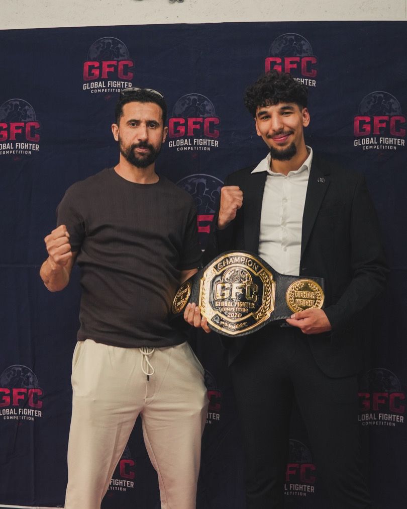 Trainer und Kämpfer mit zwei Meisterschaftsgürteln vor der Wand der Global Fighter Championship